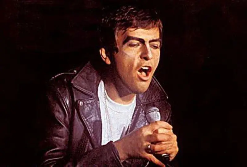 A man in brown leather jacket holding a microphone.