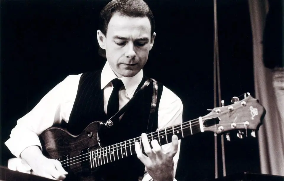 A man in vest and tie playing an electric guitar.