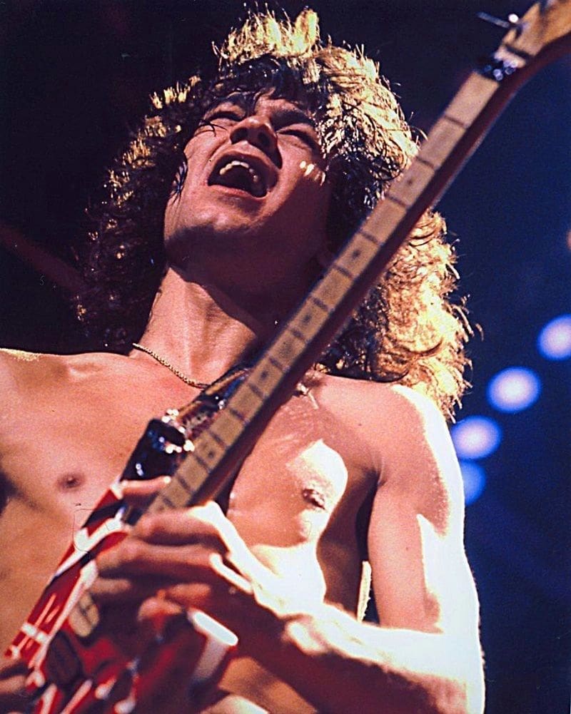 A man with long hair and bare chest holding a guitar.